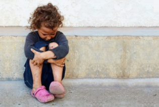 Young homeless girl sitting in the street. 