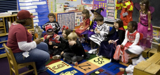 group of young students in halloween costumes gathered on the floor to listen to a teacher read a book